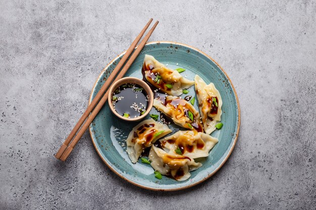 Primo piano, vista dall'alto di gnocchi tradizionali asiatici/cinesi in piastra blu con salsa di soia e bacchette su sfondo grigio pietra rustica. Autentica cucina cinese