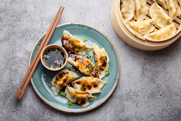 Primo piano, vista dall'alto di gnocchi tradizionali asiatici/cinesi in piatto blu con salsa di soia, bacchette e un piroscafo di bambù su sfondo grigio pietra rustica. Autentica cucina cinese