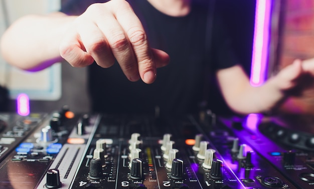 Primo piano vista delle mani del disc jockey maschio mescolando musica sul suo ponte con le mani in bilico sul disco in vinile sul giradischi e gli interruttori di controllo di notte.
