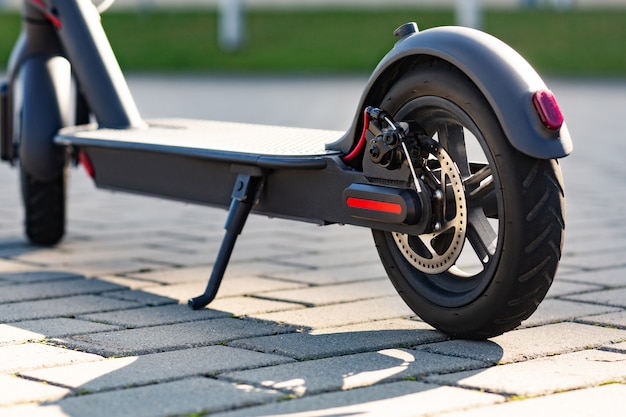 Primo piano vista di e-scooter parcheggiato sul marciapiede al paesaggio urbano sul tramonto. Trasporto urbano alla moda su moderni scooter elettrici. Concetto di mobilità eco-compatibile.