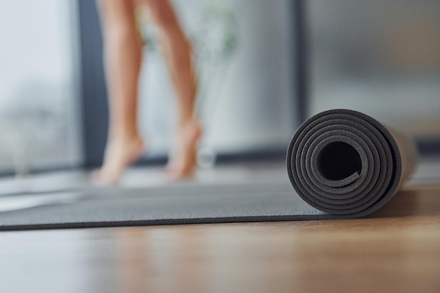 Primo piano vista focalizzata sul tappetino Giovane donna in abbigliamento sportivo e con un corpo snello ha una giornata di yoga fitness al chiuso