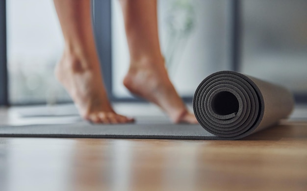 Primo piano vista focalizzata sul tappetino Giovane donna in abbigliamento sportivo e con un corpo snello ha una giornata di yoga fitness al chiuso