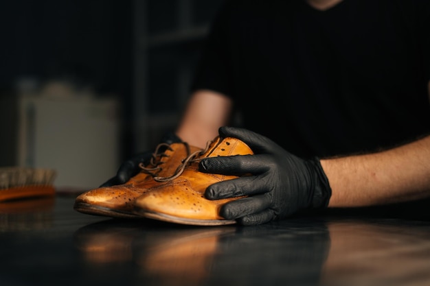 Primo piano vista laterale delle mani del calzolaio calzolaio in guanti neri che tengono vecchie scarpe di pelle marrone chiaro indossate