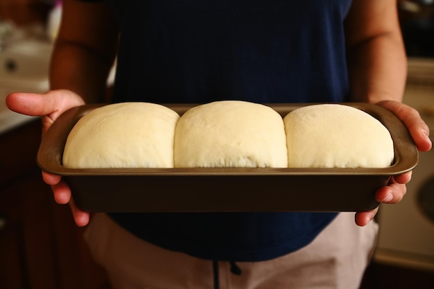 Primo piano Vista ritagliata delle mani di una casalinga che tiene un contenitore da forno con pasta lievitata adatta per il pane