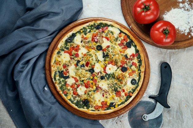 Primo piano vista su appetitosa pizza con ripieno di verdure: pesto, pomodori, mais, peperoni, cipolla sul tavolo di legno in un ristorante. Cucina italiana.