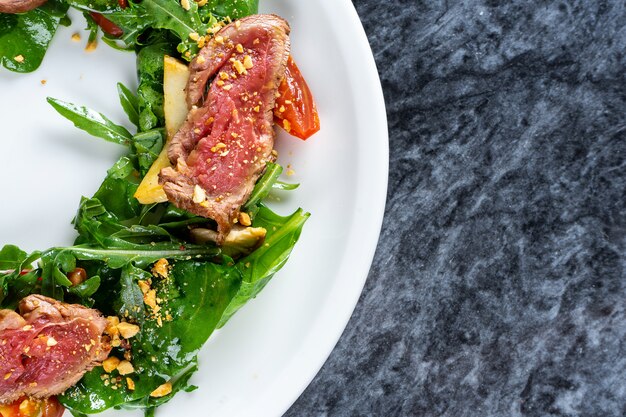 Primo piano vista sulla cucina giapponese in stile insalata Tataki con beaf spinaci, rucola. Tataki di manzo. Pranzo al ristorante per il pranzo. Piatti piatti sul tavolo di marmo.