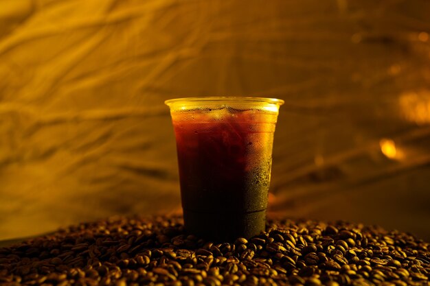Primo pianoCaffè nero ghiacciato in tazza di plastica usa e getta su chicco di caffè tostato
