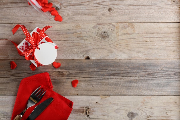 Priorità bassa della cena di San Valentino con posate regalo con cuori rossi su fondo di legno romantico