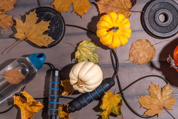 Priorità bassa di forma fisica di sport di autunno Concetto di allenamenti di caduta all'aperto Running sneakers manubri bilanciere dischi corda per saltare bottiglia d'acqua sfondo in legno con foglie autunnali zucche vista dall'alto copia spazio