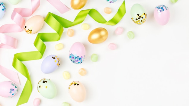 Priorità bassa festiva di Pasqua con le uova, i fiori, la caramella e i nastri decorati nei colori pastelli su bianco. Copia spazio