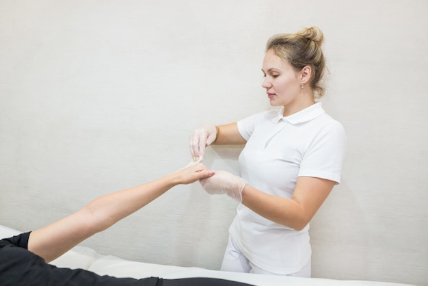 Procedura di depilazione con pasta di zucchero shugaring Il cosmetologo applica la pasta di zucchero sulla mano di una giovane donnaDepilazione delle mani femminili in un salone di bellezza
