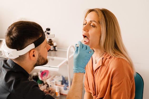 Procedura di orofaringoscopia L'otorinolaringoiatra esamina la gola della donna con la spatola Consultazione con il laringologo