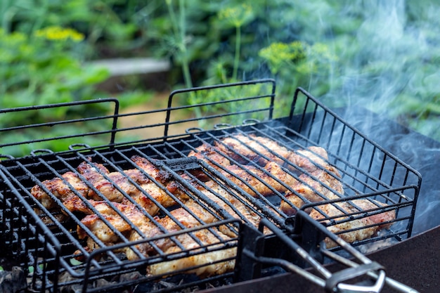 Processo che cucina bistecca carnosa su una griglia del barbecue all'aperto. Pic-nic, mangiare all'aperto. Griglia per barbecue in metallo