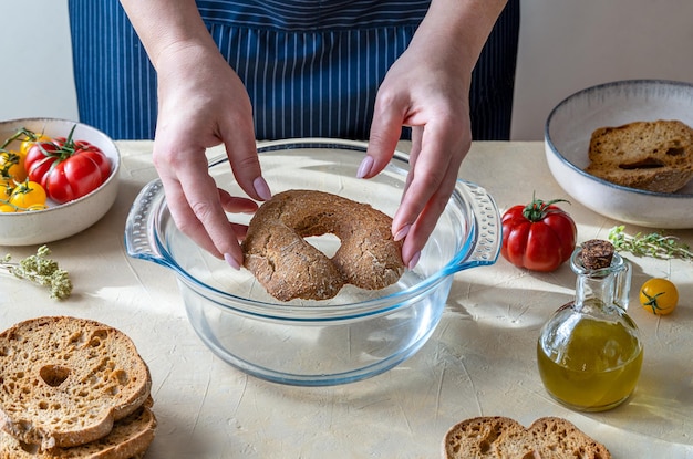 Processo di ammollo in acqua delle friselle pane tipico italiano ingredienti per guarnire pomodori rossi e gialli olio d'oliva olive e origano