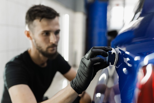 Processo di applicazione del rivestimento protettivo in ceramica sulla carrozzeria dell'auto utilizzando una spugna nei dettagli del servizio auto Il personale dell'assistenza auto applica un rivestimento ceramico per proteggere la carrozzeria dell'auto dai graffi