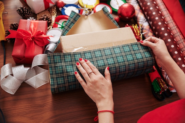 Processo di confezionamento del regalo di Natale in carta da regalo a quadri verde