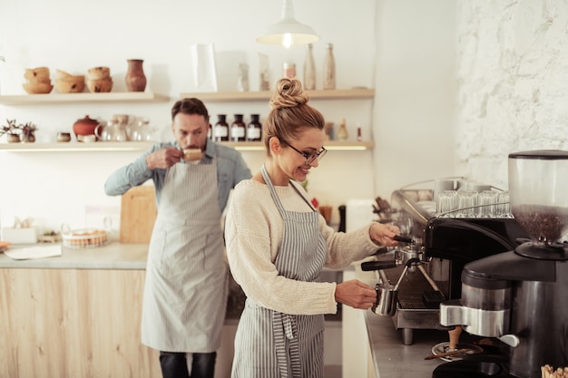 Processo di cottura a vapore. Due persone sorridenti in piedi in cucina vicino alla macchina da caffè fumanti e bevono caffè.