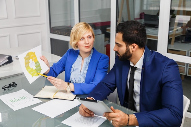 Processo di lavoro del team del manager analitico L'uomo barbuto e la donna d'affari bionda vestita con abiti lavorano con documenti all'interno dell'ufficio bianco