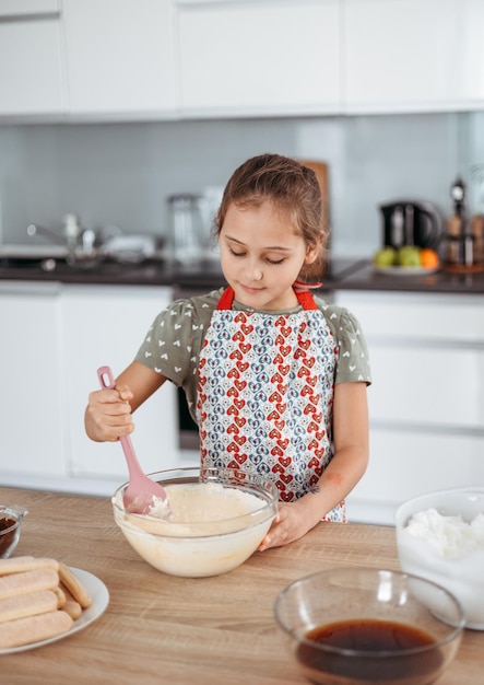 Processo di preparazione del tiramisù in cucina bambina che prepara il dessert italiano con cacao e savoiardi ricoperti di caffè espresso con crema al mascarpone passo dopo passo 6