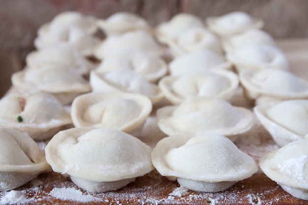 Processo di produzione di pelmeni fatti in casa (gnocchi) su tavola di legno - piatto tradizionale della cucina russa.