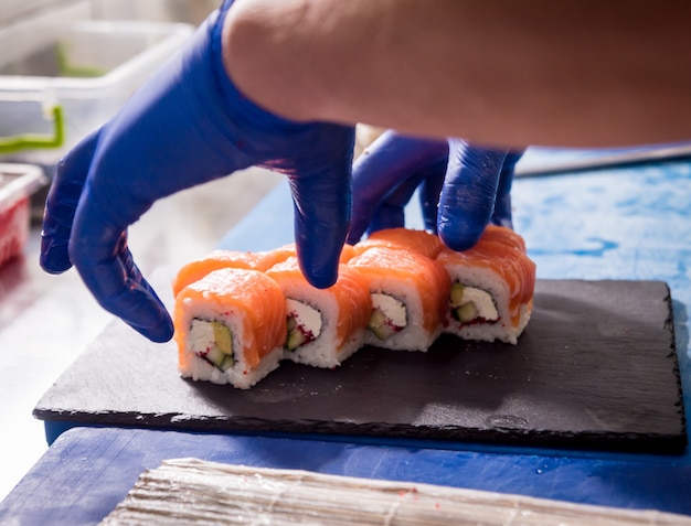 Processo di produzione di sushi e involtini alla cucina del ristorante. Mani da chef con coltello.