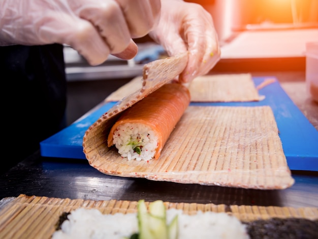 Processo di produzione di sushi e involtini alla cucina del ristorante. Mani da chef con coltello.