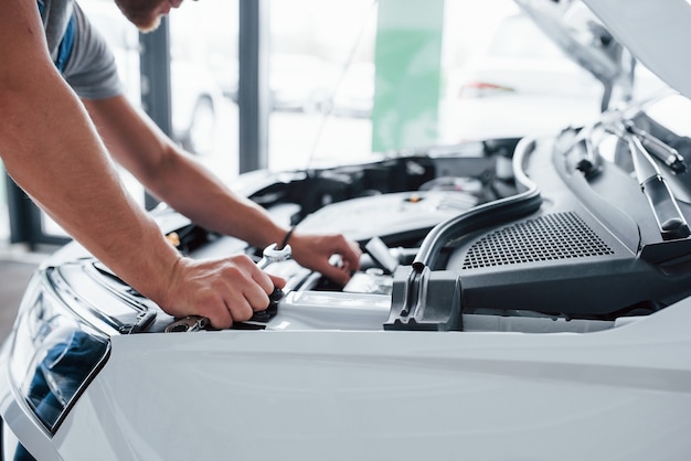 Processo di riparazione dell'auto dopo l'incidente. Uomo che lavora con il motore sotto il cofano.