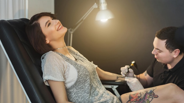 Processo di tatuaggio doloroso, giovane donna che sopporta il dolore mentre padroneggia il tatuaggio sul braccio. Modifica popolare del corpo, stile di vita moderno, spazio di copia