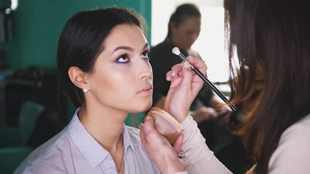 Processo di trucco al salone di bellezza per la giovane donna dai capelli neri che fa il viso per gli occhi