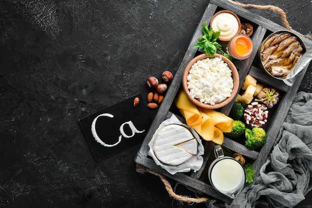 Prodotti contenenti calcio naturale: formaggio, latte, parmigiano, panna acida, pesce, mandorle, prezzemolo, aglio, broccoli. Su uno sfondo di legno nero. Vista dall'alto. Spazio di copia gratuito.