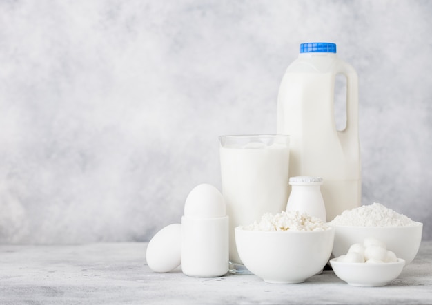 Prodotti lattiero-caseari freschi su fondo bianco. Vaso di vetro di latte, ciotola di panna acida, ricotta e farina e mozzarella. Uova e formaggio