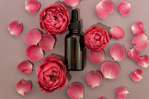 Prodotto a base di olio essenziale di rosa naturale per la cura della pelle fatto in casa su sfondo di petali di rosa rosa in flacone cosmetico di vetro scuro con contagocce per idratare la pelle. Mockup di pacchetto senza marchio.