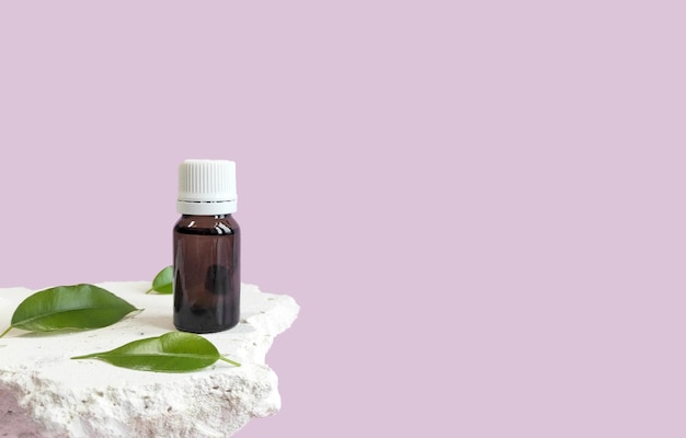 prodotto cosmetico olio aromatico su un podio di pietra e foglie verdi su sfondo rosa