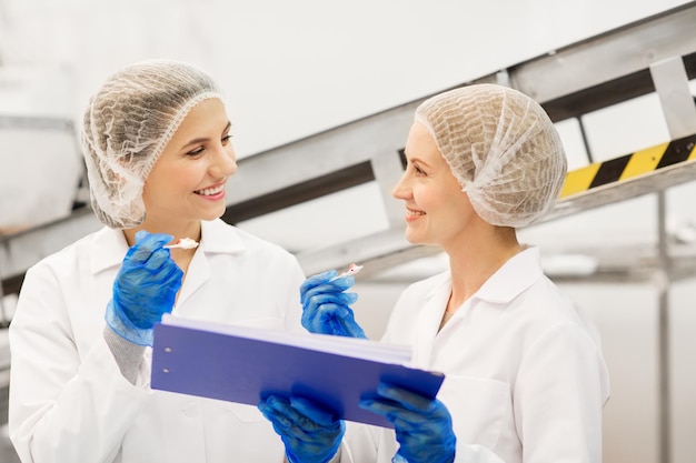 produzione alimentare, industria e concetto di persone - donne felici tecnologi con clipboard degustazione di gelato di qualità in fabbrica