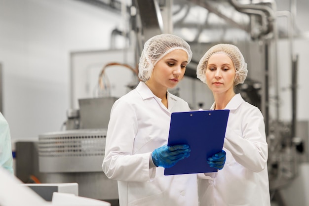 produzione, industria e concetto di persone - donne tecnologiche con clipboard nel negozio di una fabbrica di gelati