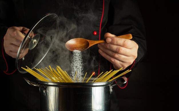 professional chef adds a spoonful of salt to a boiling pot of spaghetti free space for recipe or menu on dark background