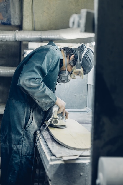 Professione, persone, falegnameria, emozione e concetto di persone: un falegname taglia una tavola con un seghetto alternativo elettrico. fabbricazione di skateboard. ha indumenti protettivi e maschera.