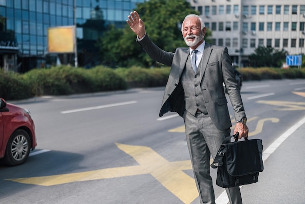 Professionista anziano con borsa per laptop che saluta per taxi in città