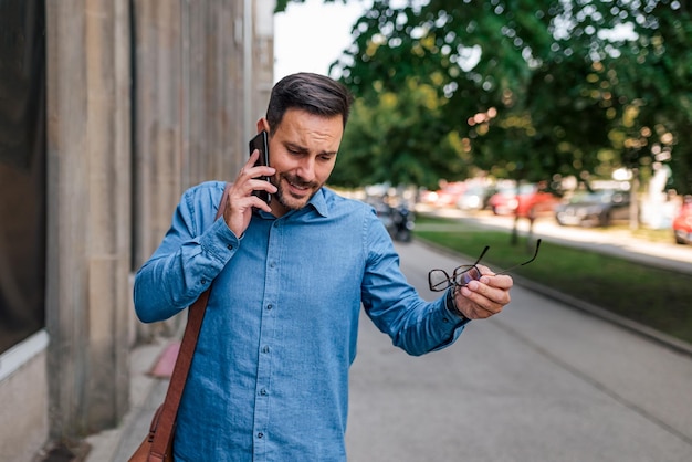 Professionista con gli occhiali che discute sul cellulare mentre si trova sul marciapiede