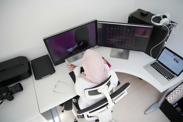 professionista creativo arabo femminile che lavora a casa in ufficio su computer desktop con vista dall'alto del monitor a doppio schermo