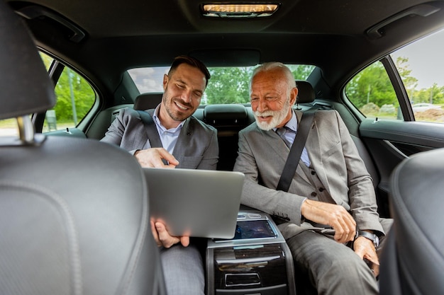 Professionisti d'affari discutono di strategie su un portatile mentre viaggiano in un'auto di lusso