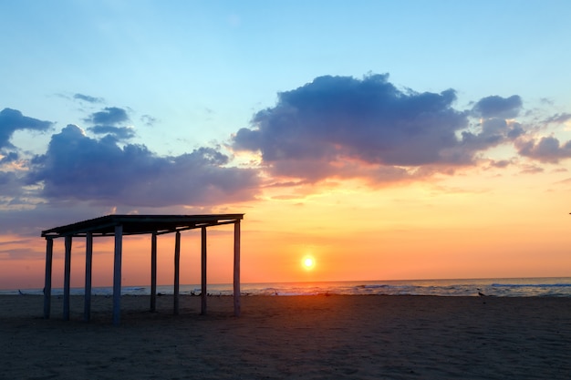 Profili il gazebo su una spiaggia sabbiosa vuota su un fondo del tramonto.