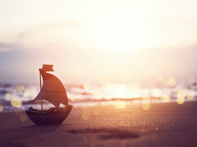 Profili il giocattolo della piccola barca sulla sabbia alla spiaggia del tramonto.