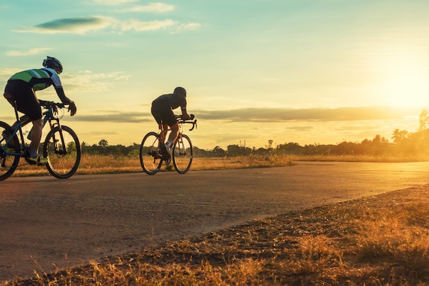 Profili il gruppo di uomini che guidano la bicicletta al tramonto.