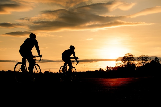 Profili il gruppo di uomini che guidano la bicicletta al tramonto.