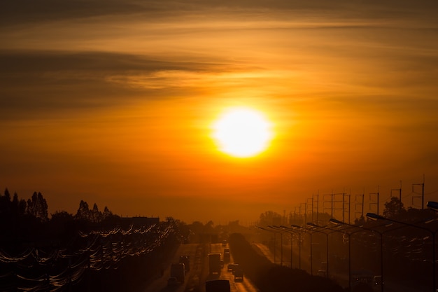 Profili il sole di mattina sulla strada con un impianto di perforazione e le linee elettriche.