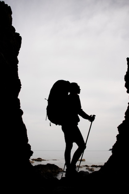 Profili la donna che sta fra le rocce sulla costa sul mare con l'escursione dello zaino