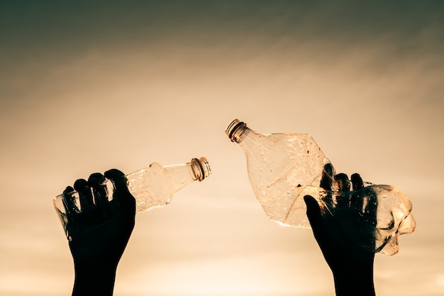 Profili la mano umana che tiene la bottiglia di plastica e l'immondizia nella natura