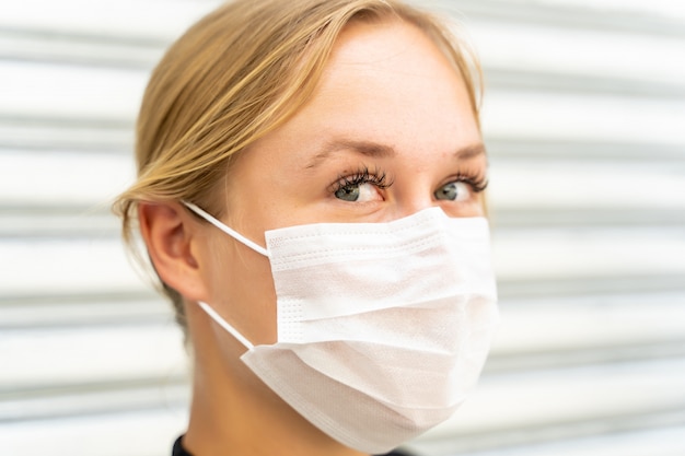 Profilo di una donna con gli occhi azzurri con una maschera sul viso che protegge dal coronavirus