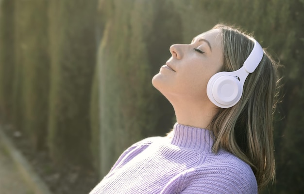 Profilo di una donna rilassante che medita con cuffie wireless nel parco in una giornata di sole